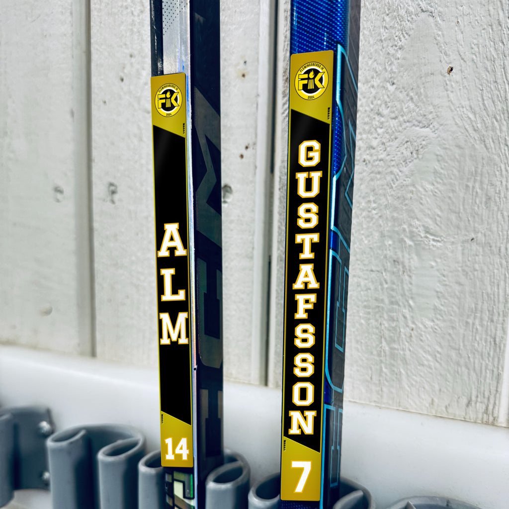 Flemingsbergs IK stick stickers applied to two hockey sticks in a rack