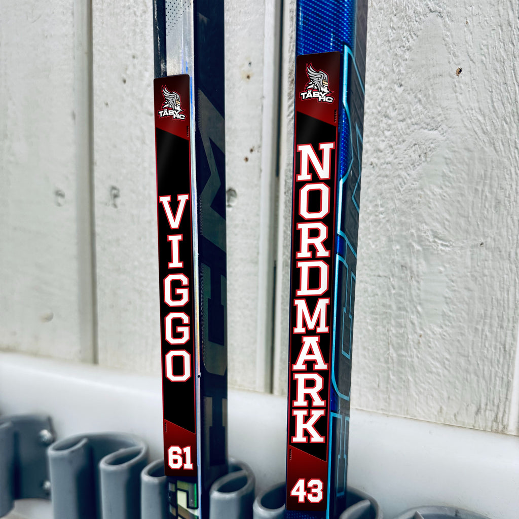 Täby HC stick stickers applied to two hockey sticks in a rack
